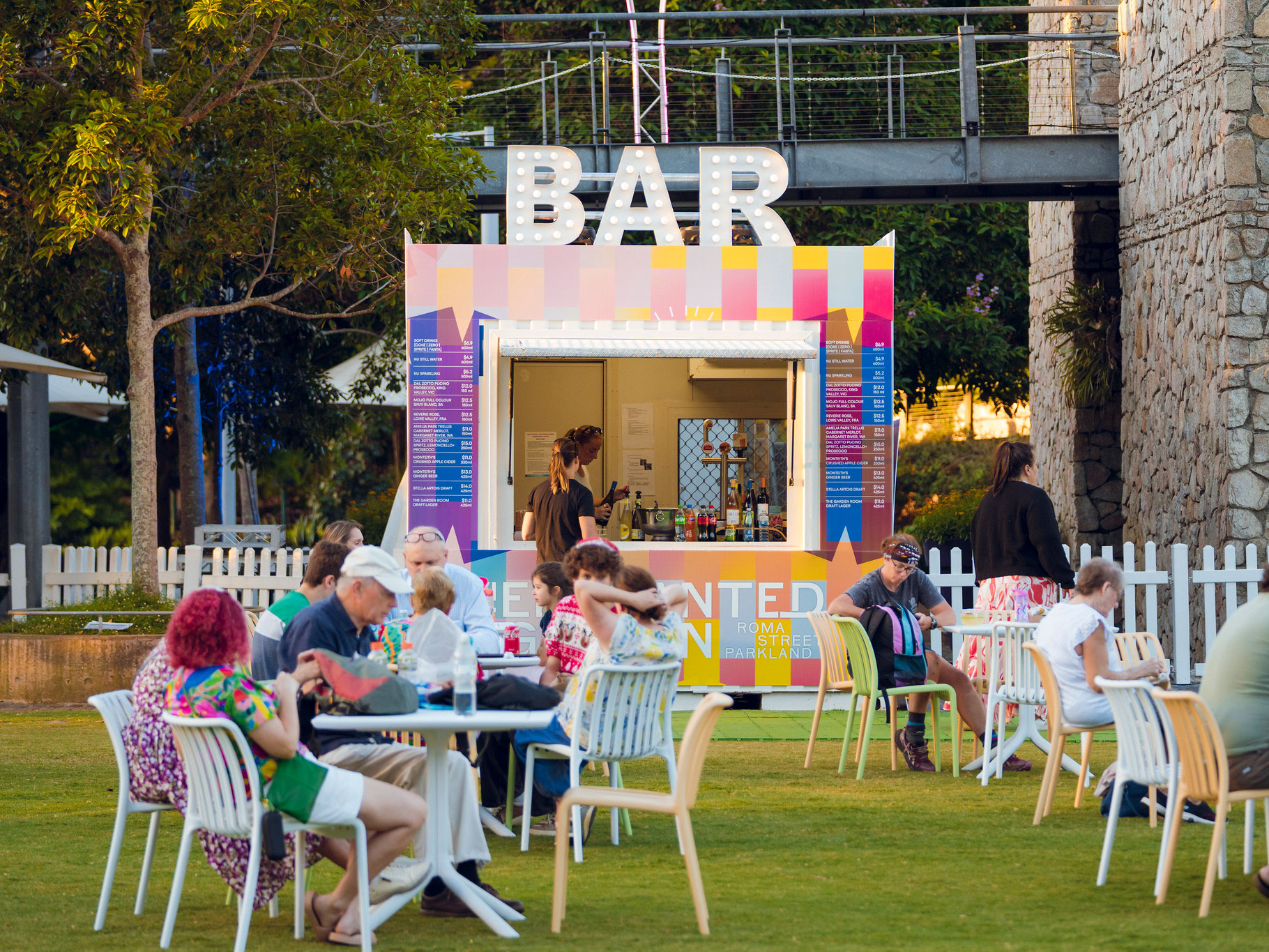 Lit outdoor bar and some tables and chairs with people sat at them on Celebration Lawn